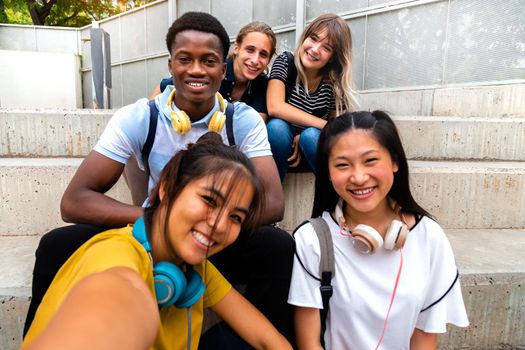 Happy smiling teen multiracial group of students looking at camera take selfie sitting on steps outside. Education and social media concepts.