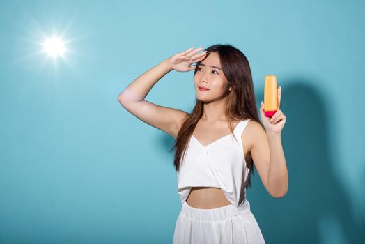 Beautiful Asian young woman holding body lotion on hand in studio shot isolated on blue background, Brunette female hold cream sunblock bottle, tube of sunscreen, Beauty cosmetics facial treatment