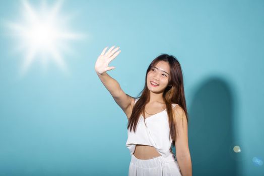 Asian young woman hand up cover face protect sun light and UV smile in studio shot isolated on blue background, female raising arm and hand in protection and block sunshine, sunscreen cream advertise