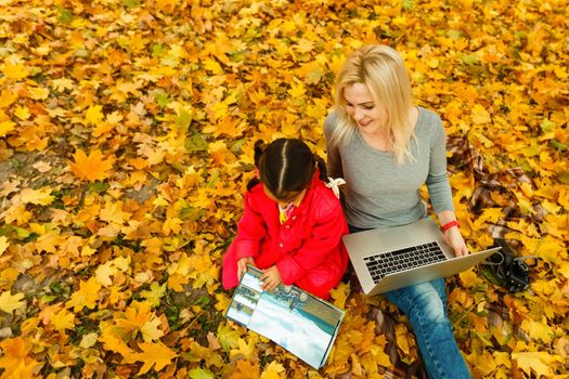 mother and daughter work on laptop outside in autumn