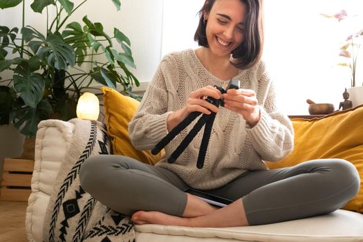 Young happy caucasian woman preparing mini tripod to start recording video with mobile phone at home. Social media concept.