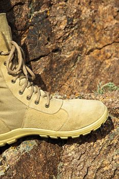 Comfortable high-laced leather hiker's boot in a rocky area with a rock in the background. Copy space, vertical.