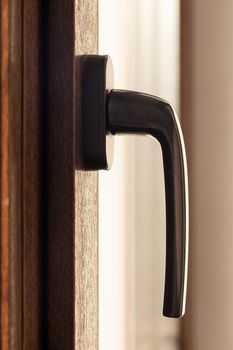 Window handle on a brown metal-plastic window, side view, vertical.