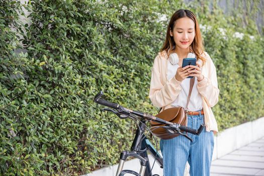 Asian young woman commute on smartphone with bicycle on summer in park countryside outdoor, Happy female smiling walk at street with her bike on city road and cellphone with mobile phone