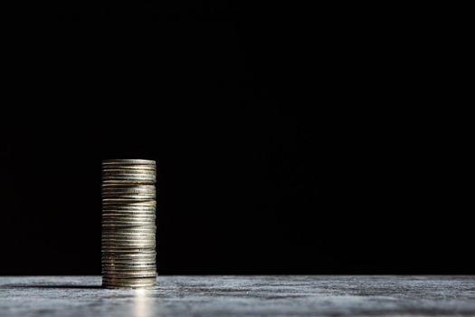Stack of coins on grey table and black background. Start-up capital concept with copy space.