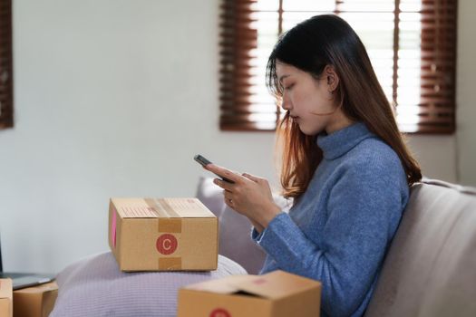 Portrait of Young Asian woman chatting with her friend and checking social media by smartphone sitting on couch. Lifestyle concept.