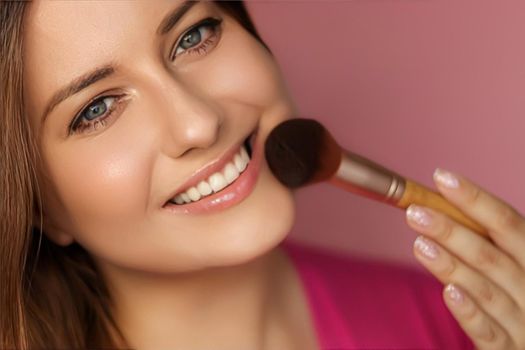 Beautiful young woman applying cosmetic powder product with make-up bamboo brush, beauty, makeup and skincare cosmetics model face portrait on pink background, closeup