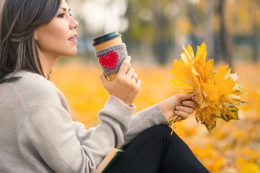 Young mixed race woman drinking coffee in autumn park.