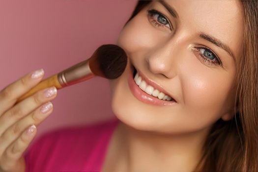 Beautiful young woman applying cosmetic powder product with make-up bamboo brush, beauty, makeup and skincare cosmetics model face portrait on pink background, closeup