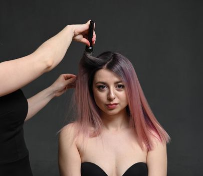 Hairdresser divides long hair into sections with the comb of a young caucasian blonde woman in a hair salon