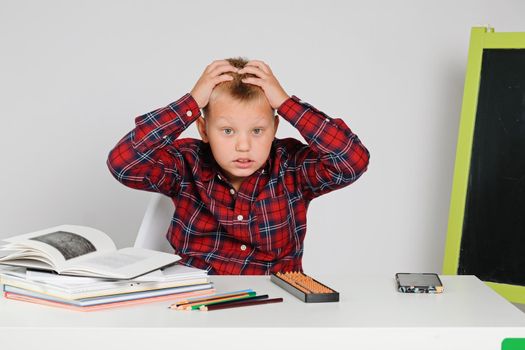 Little school boy feeling panic frustrated upset doing school homework at the table.