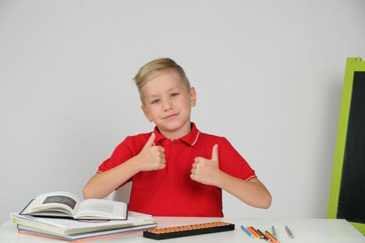 Happy little school boy feeling happy satisfied doing school homework at the table, show thumb up