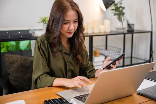 Asian business woman using laptop checking smartphone indoors home office, Happy female smile working multiple devices with computer and mobile phone, beautiful people pay digital online on desk