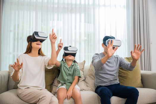 Asian family wear vr glasses headsets sitting on sofa in living room, game entertainment innovation technology, Happy family have mother father and daughter watching movie or playing video game