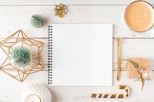 Top view Desktop Christmas notepad with mockup blank paper. Flat lay on white wooden table background with planner, coffee cup, tree brunch, Christmas eco nature decoration, notebook and stationery.