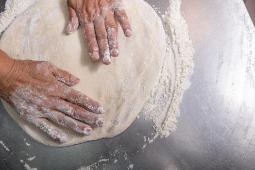 Woman making pizza dough on stainless steel counter. Motion blur