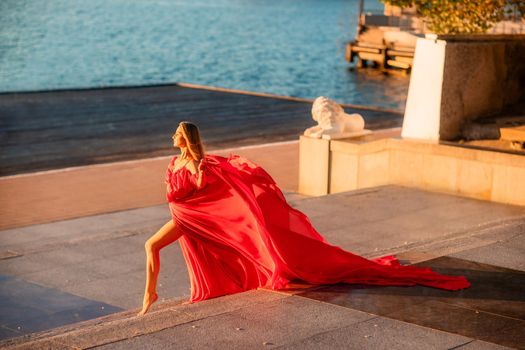 A woman in a long red dress against the backdrop of sunrise, bright golden light of the sun's rays. The concept of femininity, harmony