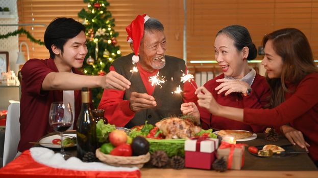 Happy family with sparklers enjoying Christmas eve dinner together in comfortable home. Celebration, holidays and Christmas concept.