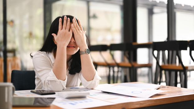 Overworked businesswoman holding covering her face, feeling strong headache, exhausted from overwork or stress at work.