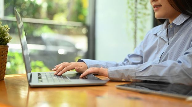 Side view young woman employee hands typing business email on her laptop computer.