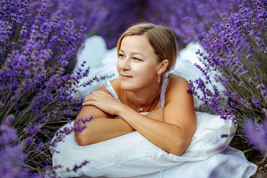 A middle-aged woman lies in a lavender field and enjoys aromatherapy. Aromatherapy concept, lavender oil, photo session in lavender.