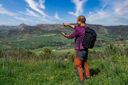 man with backpack man orienting himself in the mountains with his mobile phone, mountain landscape in the background and cloudy sky