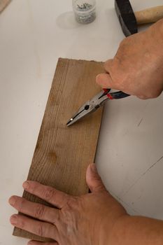 close-up of a woman's hands pulling a nail out of a wooden board.