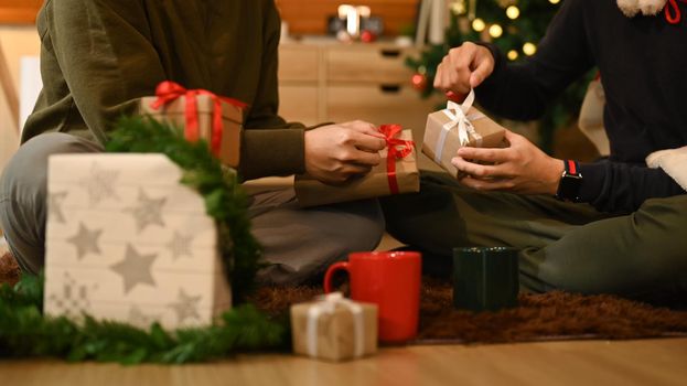 Cropped shot of two man celebrating Christmas, New Year at home together and exchange presents.