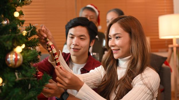 Happy young couple enjoying decorating Christmas tree, preparing for celebrating winter holidays together.