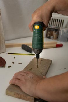 hands with electric screwdriver screwing screws into wood