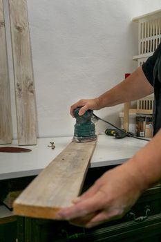 hands with electric sanding machine sanding wood in a workshop
