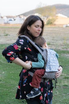 Young mother with her toddler kid boy on back in ergonomic baby carrier in autumn nature. Active mother concept