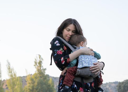 Young mother with her toddler kid boy on back in ergonomic baby carrier in autumn nature. Active mother concept