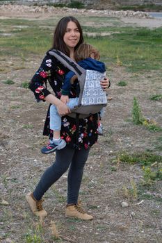 Young mother with her toddler kid boy on back in ergonomic baby carrier in autumn nature. Active mother concept