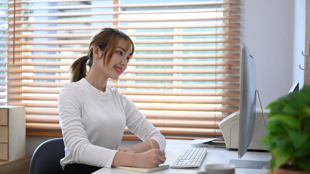 Beautiful young creative woman freelancer working online from home, watching online webinar on computer.