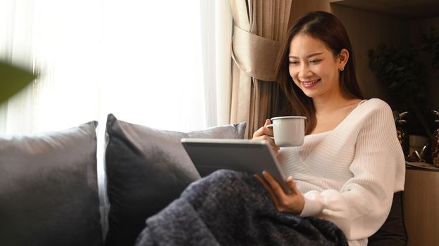Happy woman resting on comfortable couch and using digital tablet, enjoy stress free peaceful mood at the morning.