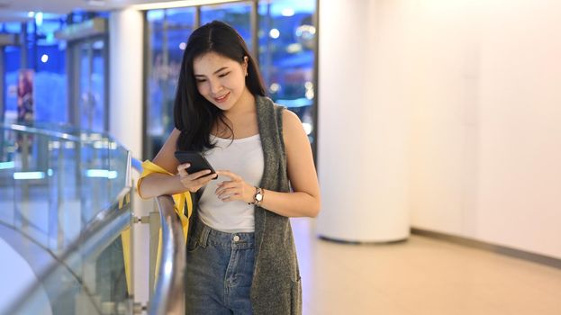 Young woman with shopping bags using mobile phone while standing in department store. Black Friday, shopping, lifestyle concept.