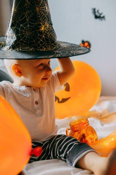 Children's Halloween - a boy in a witch hat and a carnival costume with airy orange and black balloons at home. Ready to celebrate Halloween.