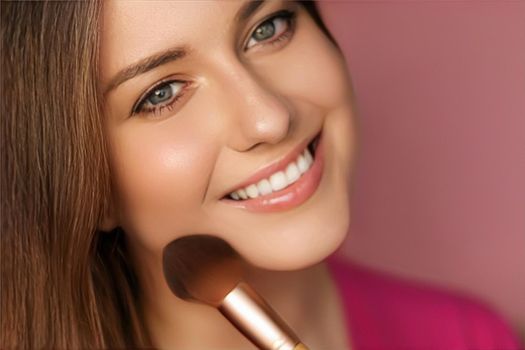 Beautiful young woman applying cosmetic powder product with make-up bamboo brush, beauty, makeup and skincare cosmetics model face portrait on pink background, closeup