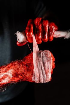 A man covered in blood bandages his hands