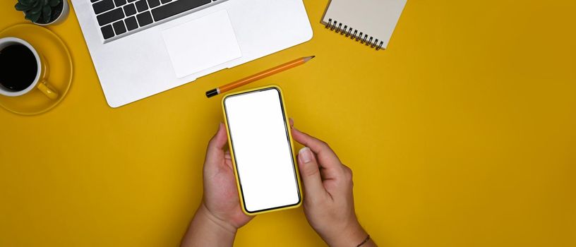 Above view man holding smart phone on yellow background.