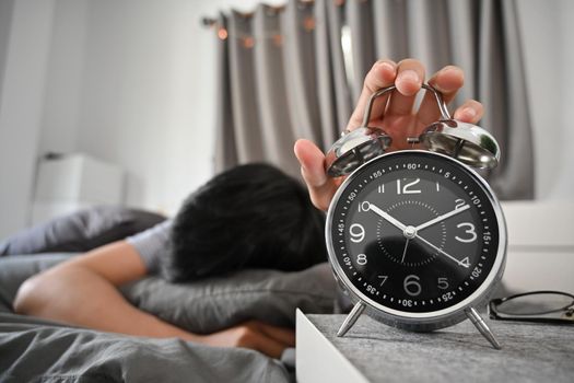 Young man lying on bed and turning off an alarm clock in the morning.