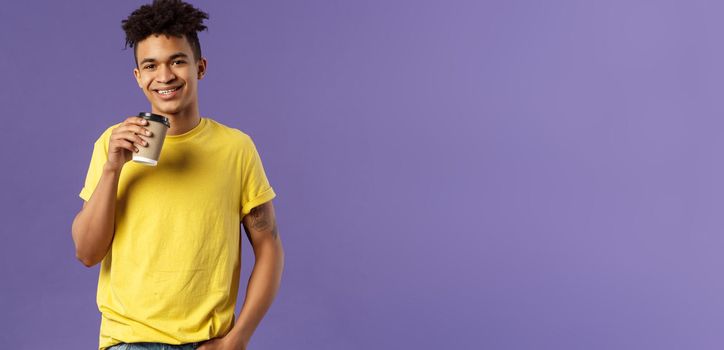 Portrait of good-looking young male student with dreads, tattoos, casually drinking coffee from take-away cup, visit favorite cafe, smiling cheerful, enjoying perfect warm sunny day.