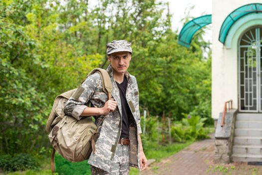 Photo of soldier in camouflaged uniform holding olive colored backpack.