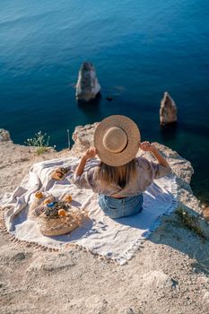 Woman on a picnic overlooking the sea. Dressed in a beige top denim shorts, sits on a mountain and looks at the sea.