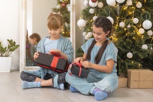 Two cute little girls under Christmas tree. Children under Christmas tree with gift boxes. New Year's decorations. Sisters.