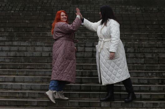 Two plus size women in white and brown coats are emotionally posing. A brunette and a brown-haired woman advertise clothes.