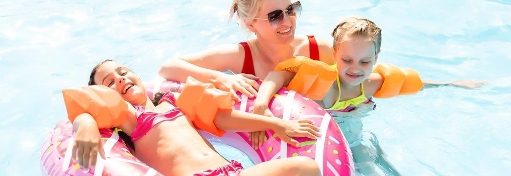 Happy family in the pool, having fun in the water, mother with kids enjoying aqua park, beach resort, summer holidays, vacation concept.