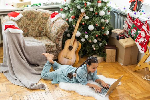 little girl sitting, looking at a laptop with a smile before Christmas.