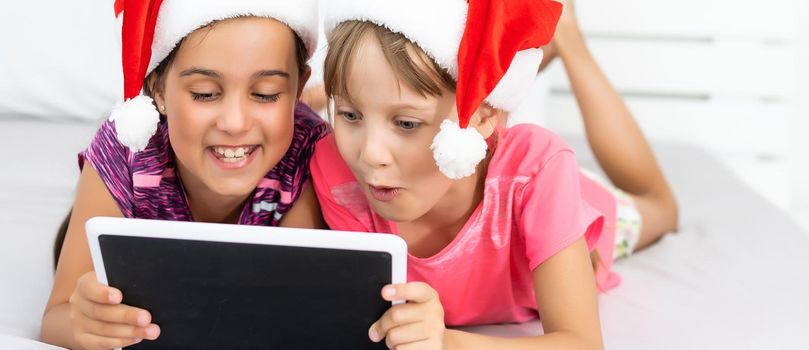 Excited small sister kids have fun browsing playing on modern tablet gadget together. Happy little girl children watch video on pad device, enjoy family winter holidays at home